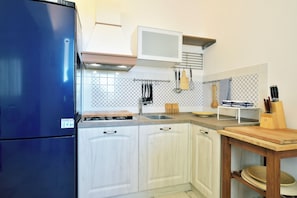 Eine Küche mit weißen Schränken, einem blauen Kühlschrank, einem Holztisch und einer gefliesten Spritzschutzwand.