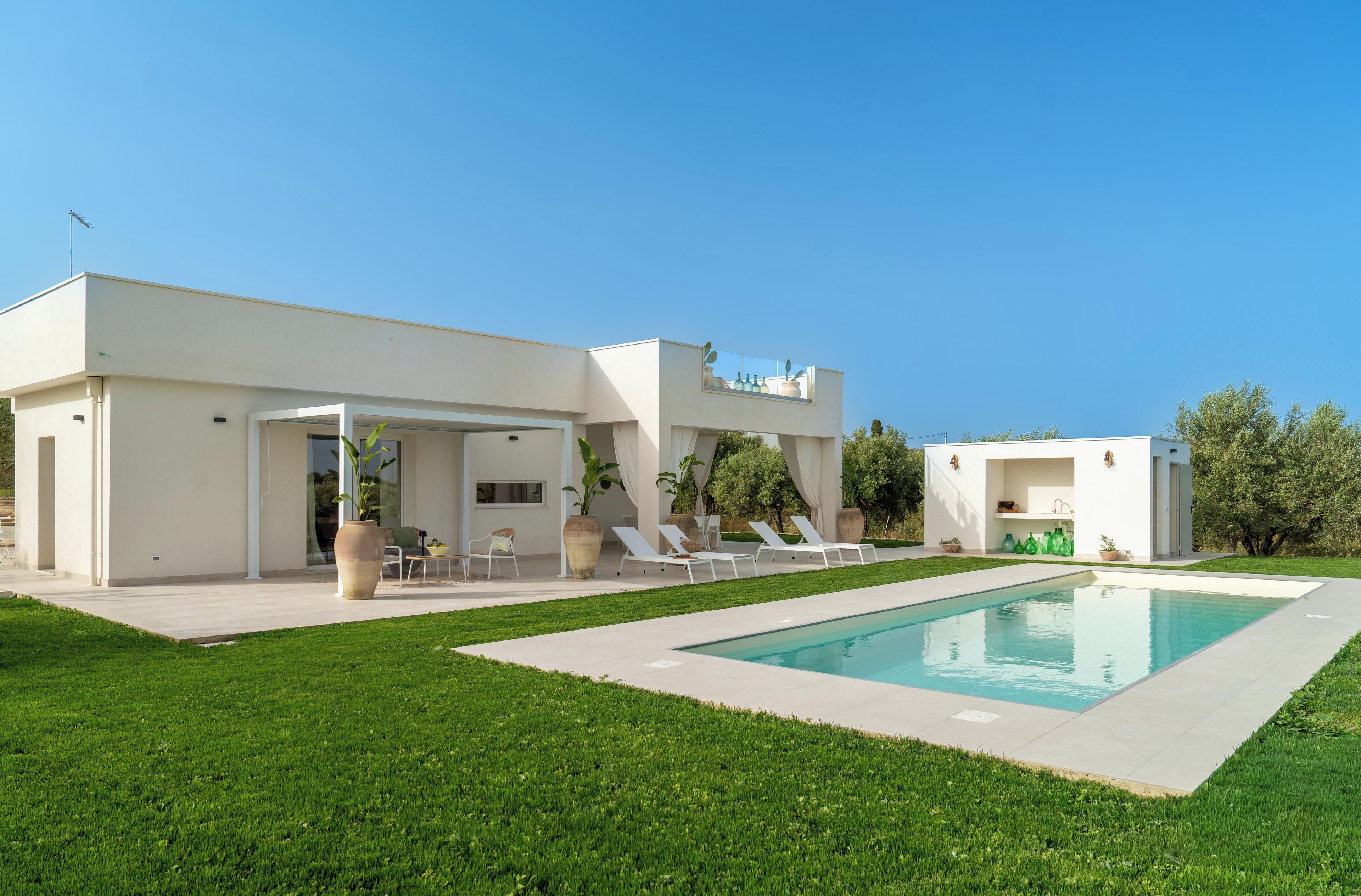 Une maison moderne dotée d’une piscine, d’un espace salon extérieur et d’un patio couvert.