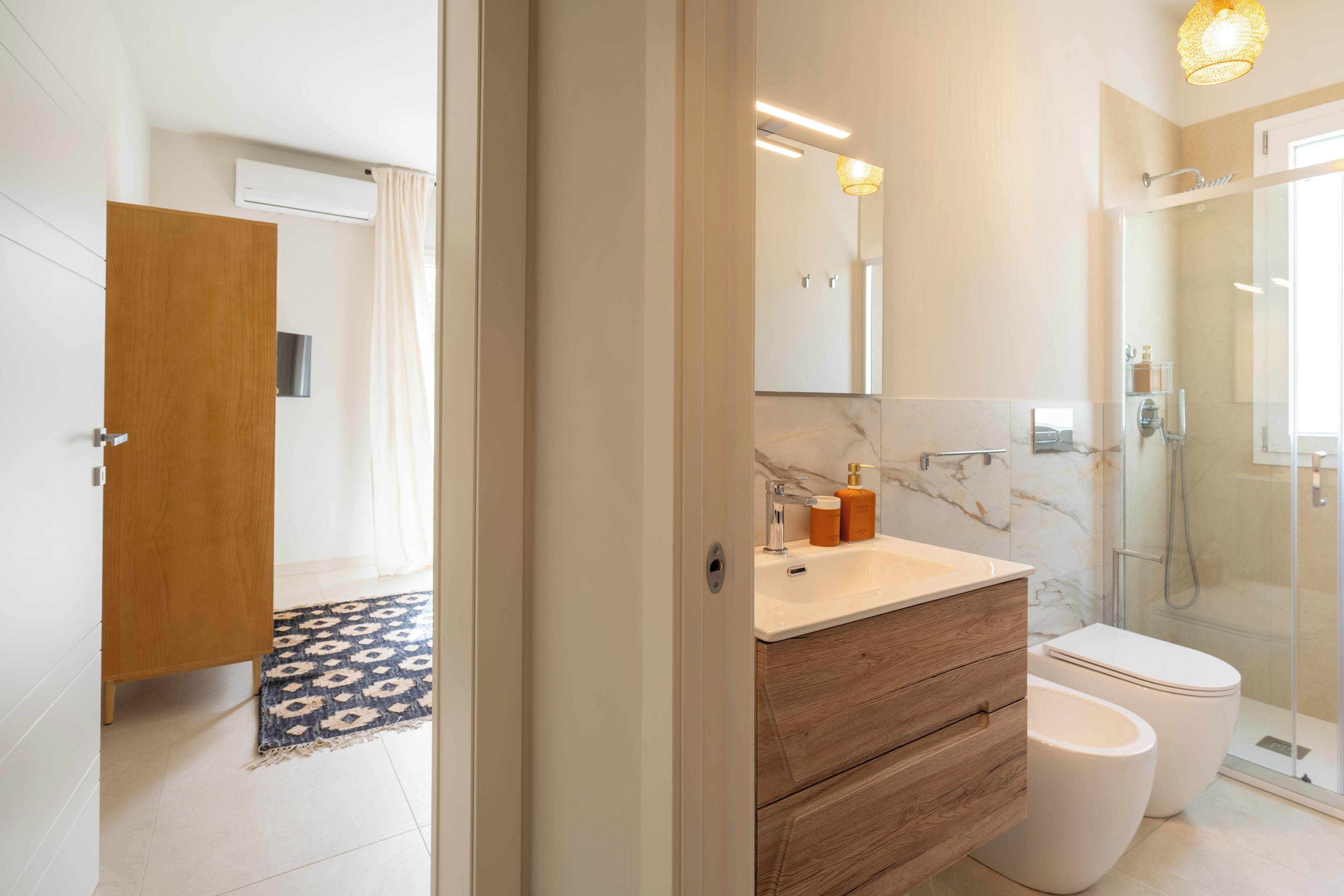 A modern bathroom with a marble vanity, a glass shower enclosure, and a wooden door.