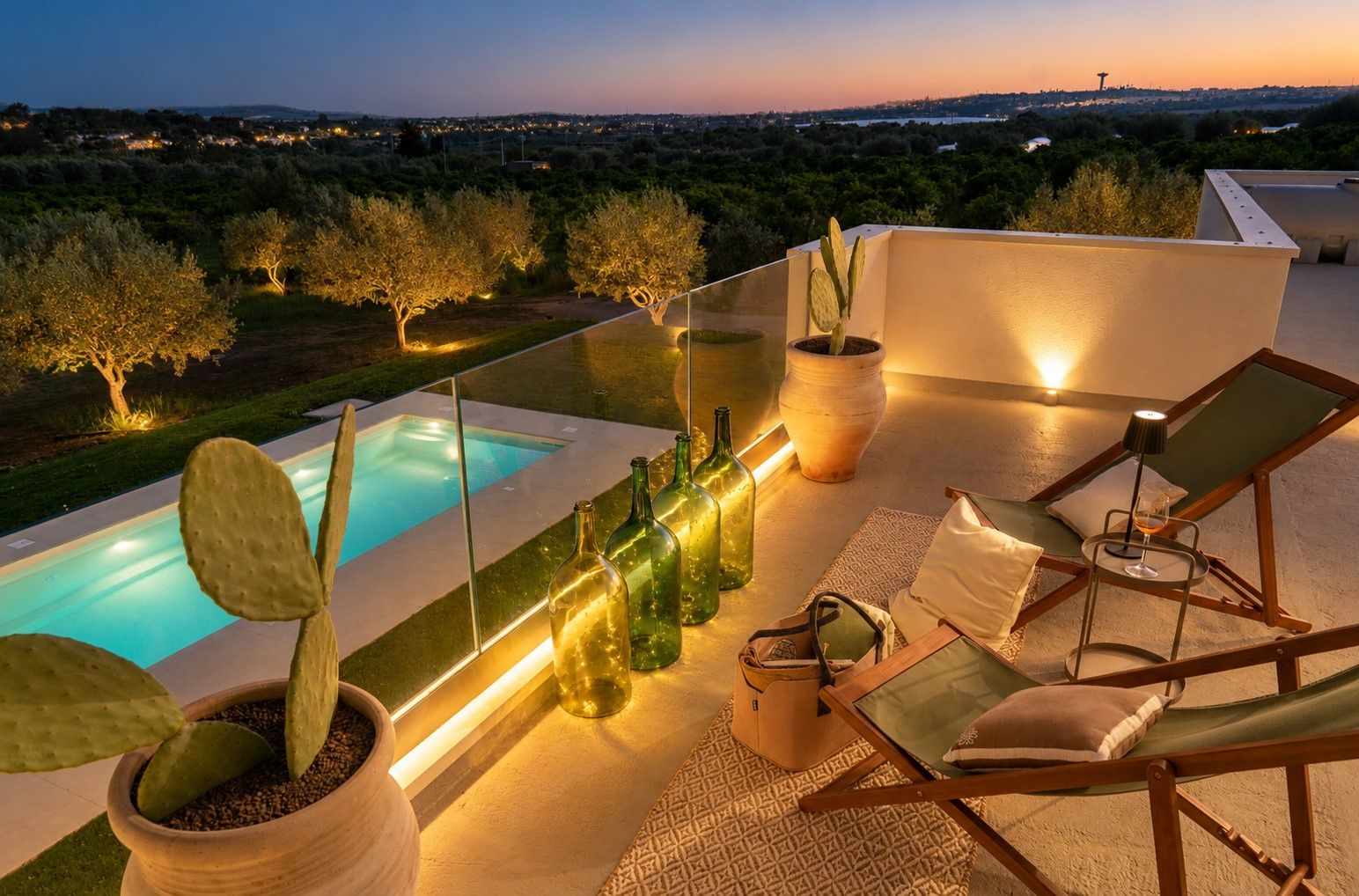 A rooftop terrace with a pool, lounge chairs, potted plants, and a view of the landscape.