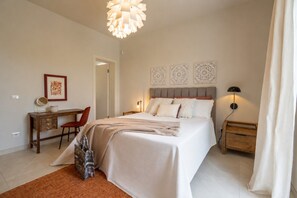 Une chambre à coucher comprenant un lit, une table de chevet, une lampe, un bureau, une chaise et une œuvre d’art accrochée au mur.