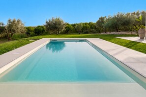 Une piscine rectangulaire à l’eau d’un bleu limpide, entourée d’une pelouse bien entretenue et d’arbres.