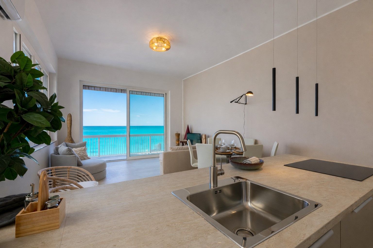 A modern kitchen with a large island, a sink, and a dining area with a view of the ocean.
