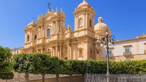 A large, historic building with multiple domes and towers, likely a cathedral or church, surrounded by a well-maintained hedge and a metal fence. - Marzamemi on the Beach Sicilymyhome (Pachino)
