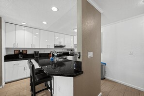A modern kitchen with white cabinets, a black countertop, and stainless steel appliances. - Bay View Condo Near SeaWorld, San Diego (San Diego)