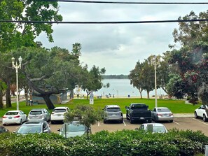 A parking lot with cars, a grassy area, and a body of water in the background. - Bay View Condo Near SeaWorld, San Diego (San Diego)