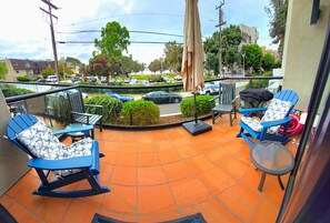 A balcony with blue chairs, a glass table, and a view of a street with cars and buildings. - Bay View Condo Near SeaWorld, San Diego (San Diego)