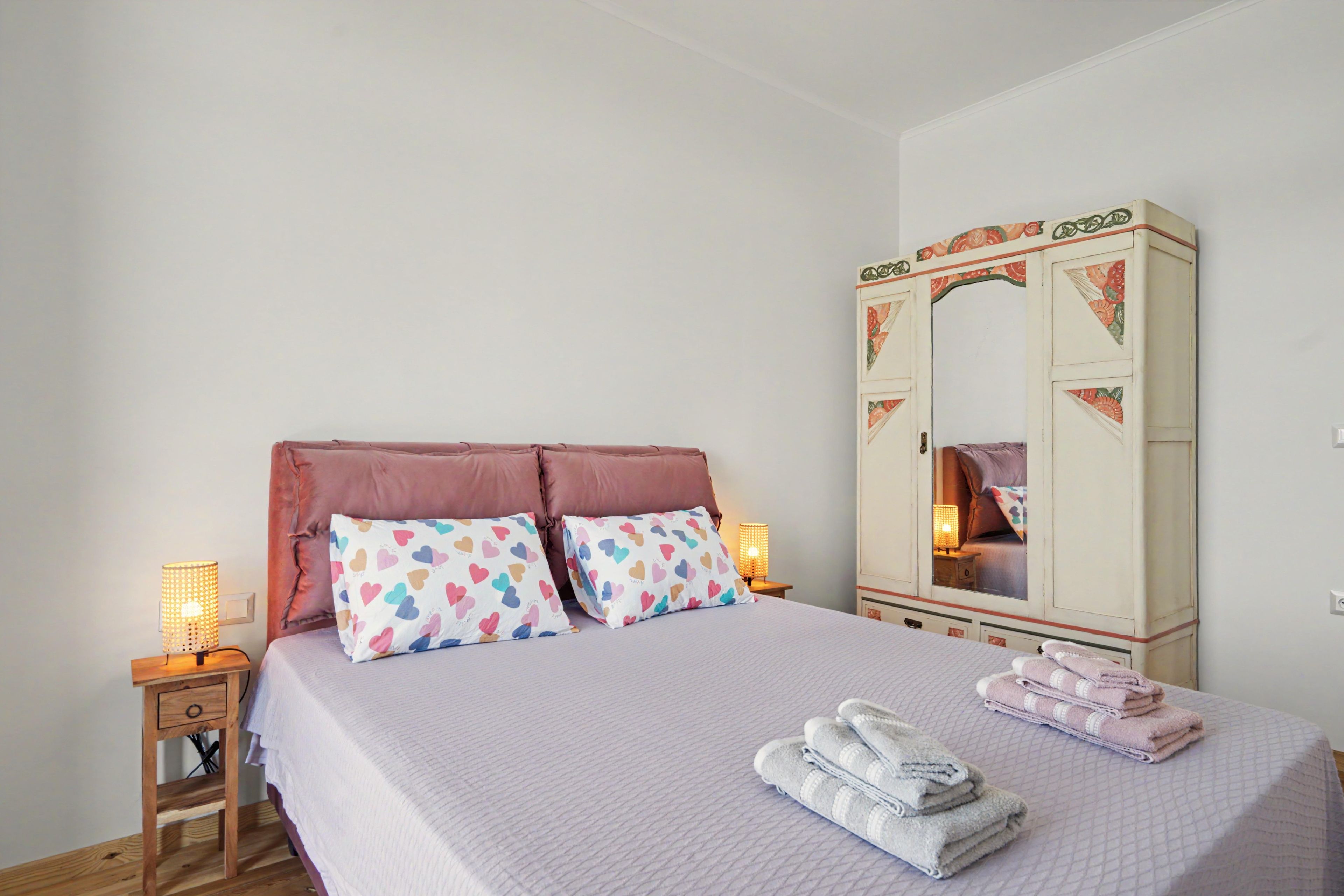 A bedroom with a bed, two bedside lamps, a wardrobe, and a mirror.
