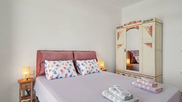 A bedroom with a bed, two bedside lamps, a wardrobe, and a mirror.