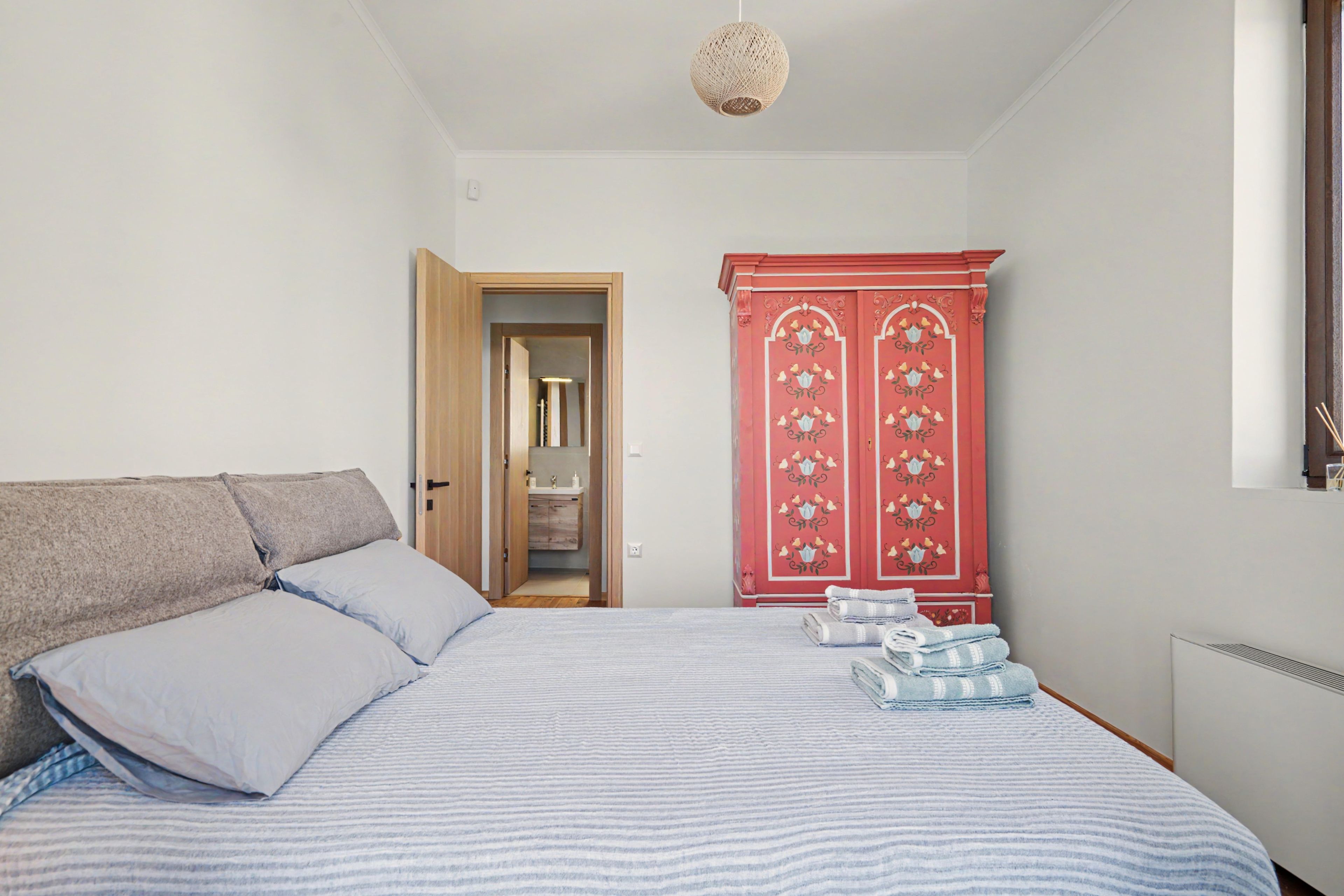 A bedroom with a bed, pillows, a wardrobe, and a hanging light fixture.