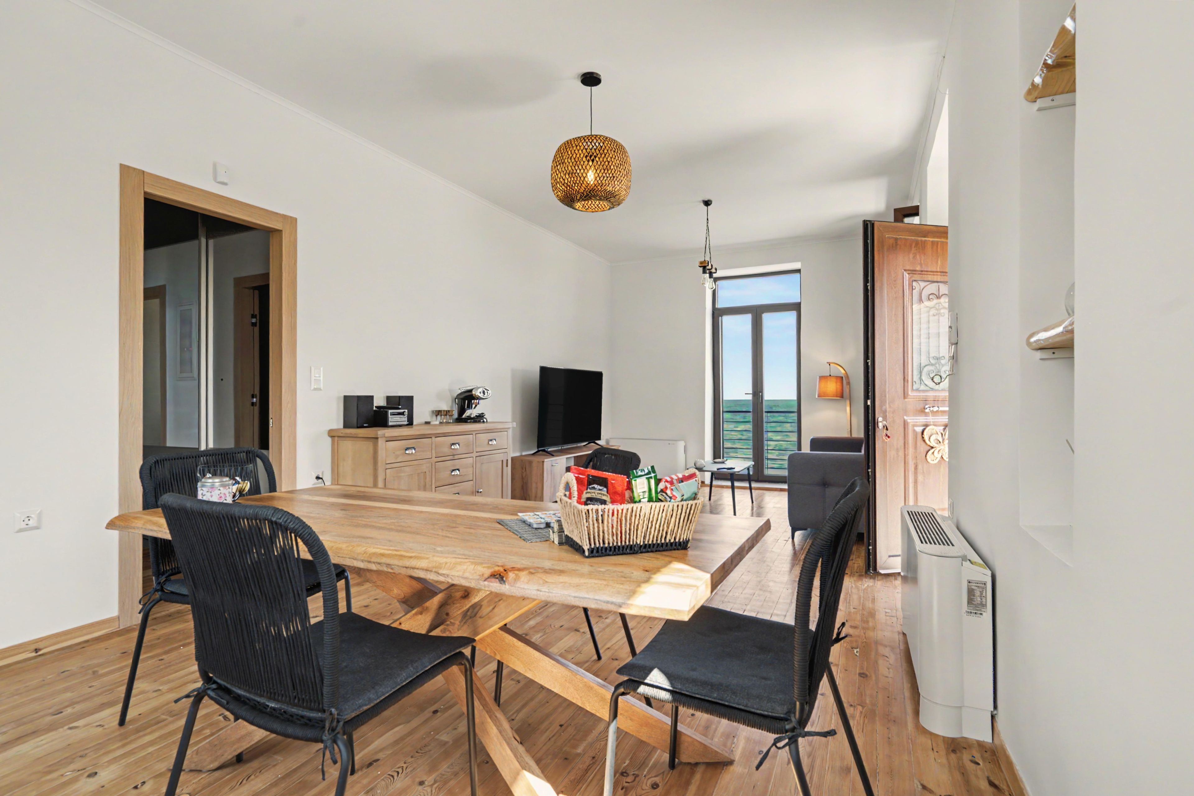 A modern kitchen with a wooden table and chairs, a television, and a large window.