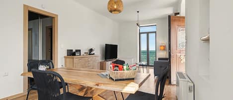 A modern kitchen with a wooden table and chairs, a television, and a large window.