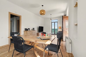 A modern kitchen with a wooden table and chairs, a television, and a large window.