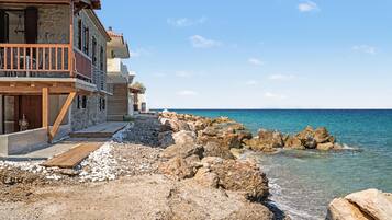 A coastal building with a stone facade, wooden deck, and a view of the sea.