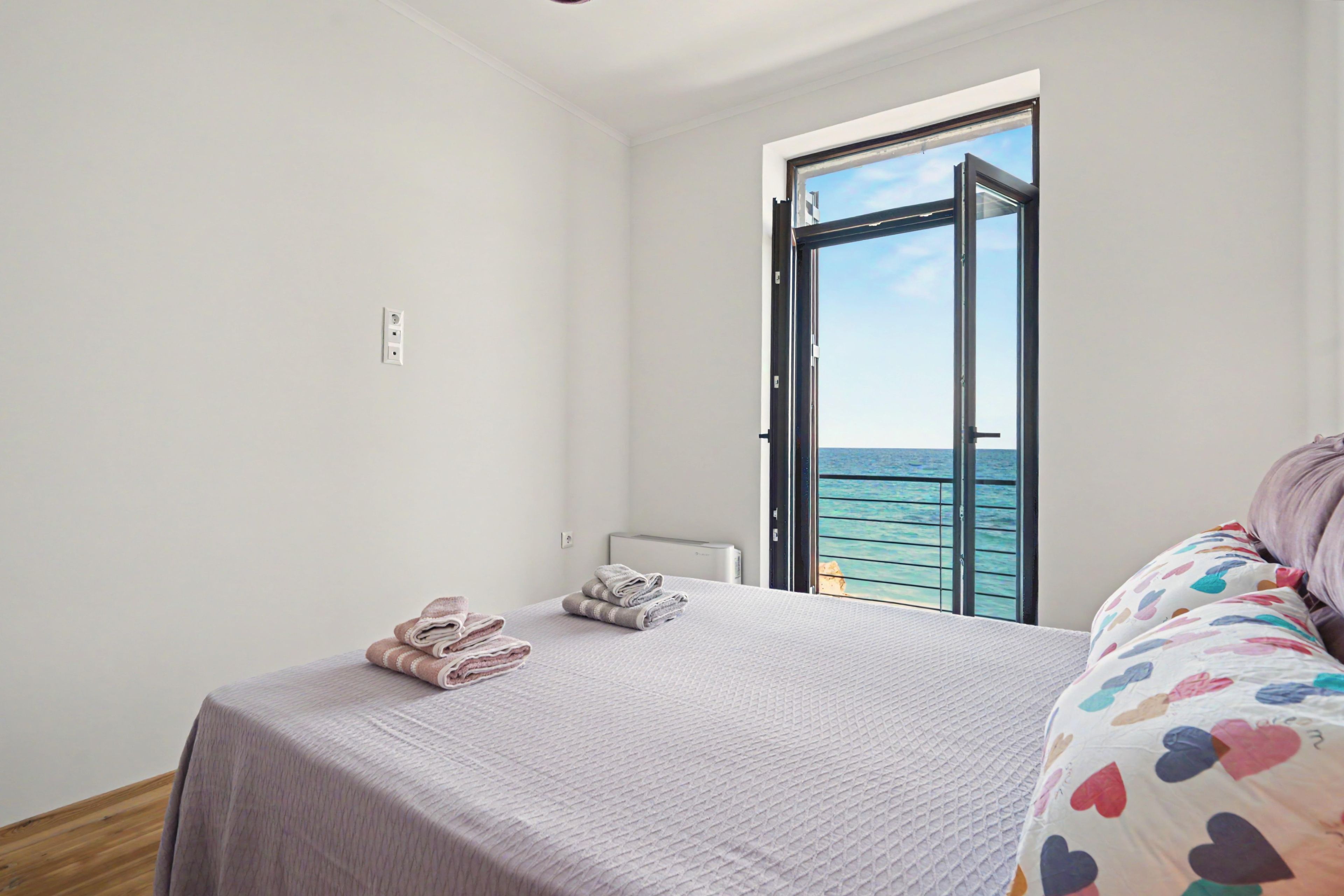 A bedroom with a bed, a window, and a view of the sea.