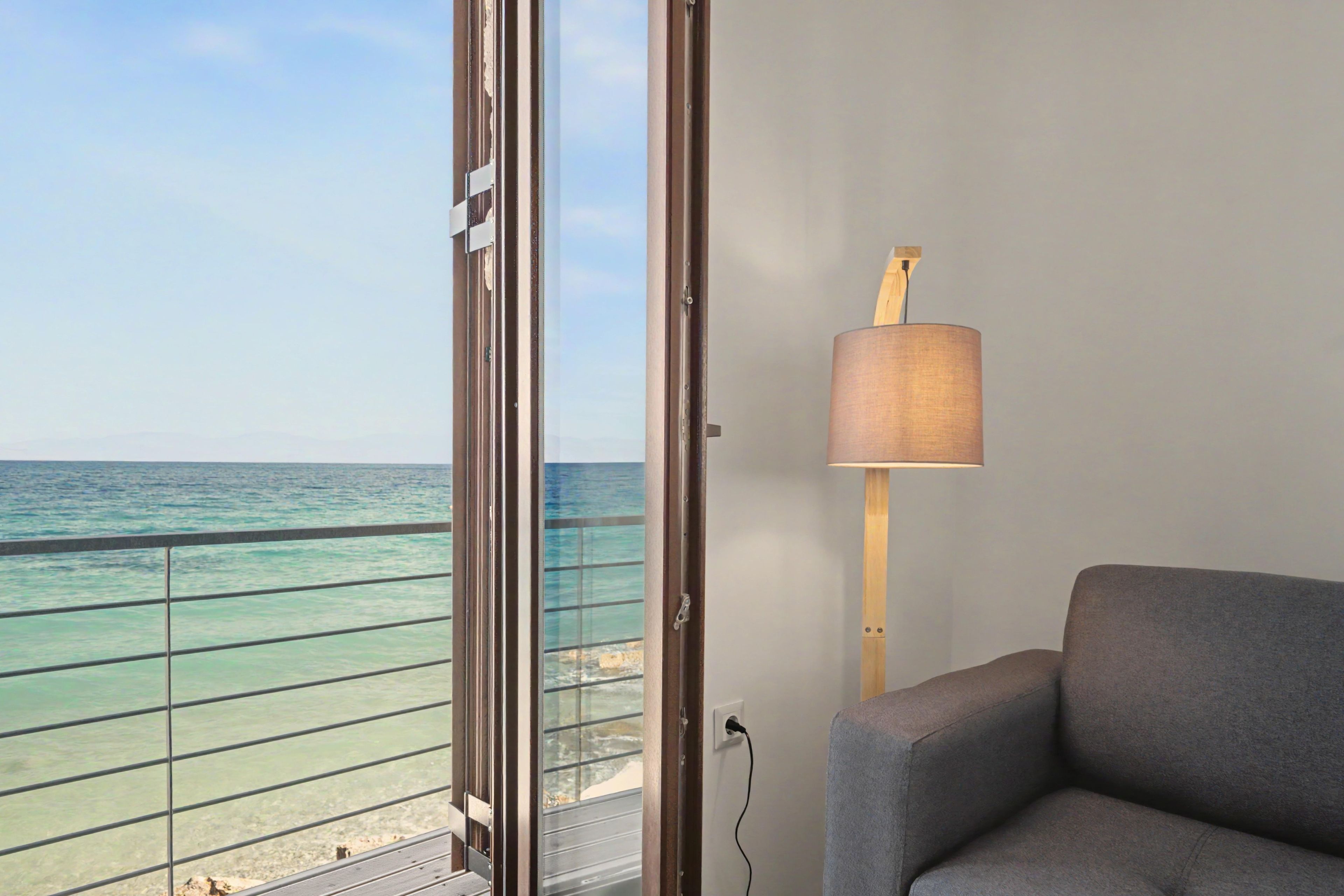 Une pièce avec vue sur la mer, un canapé gris et une lampe.