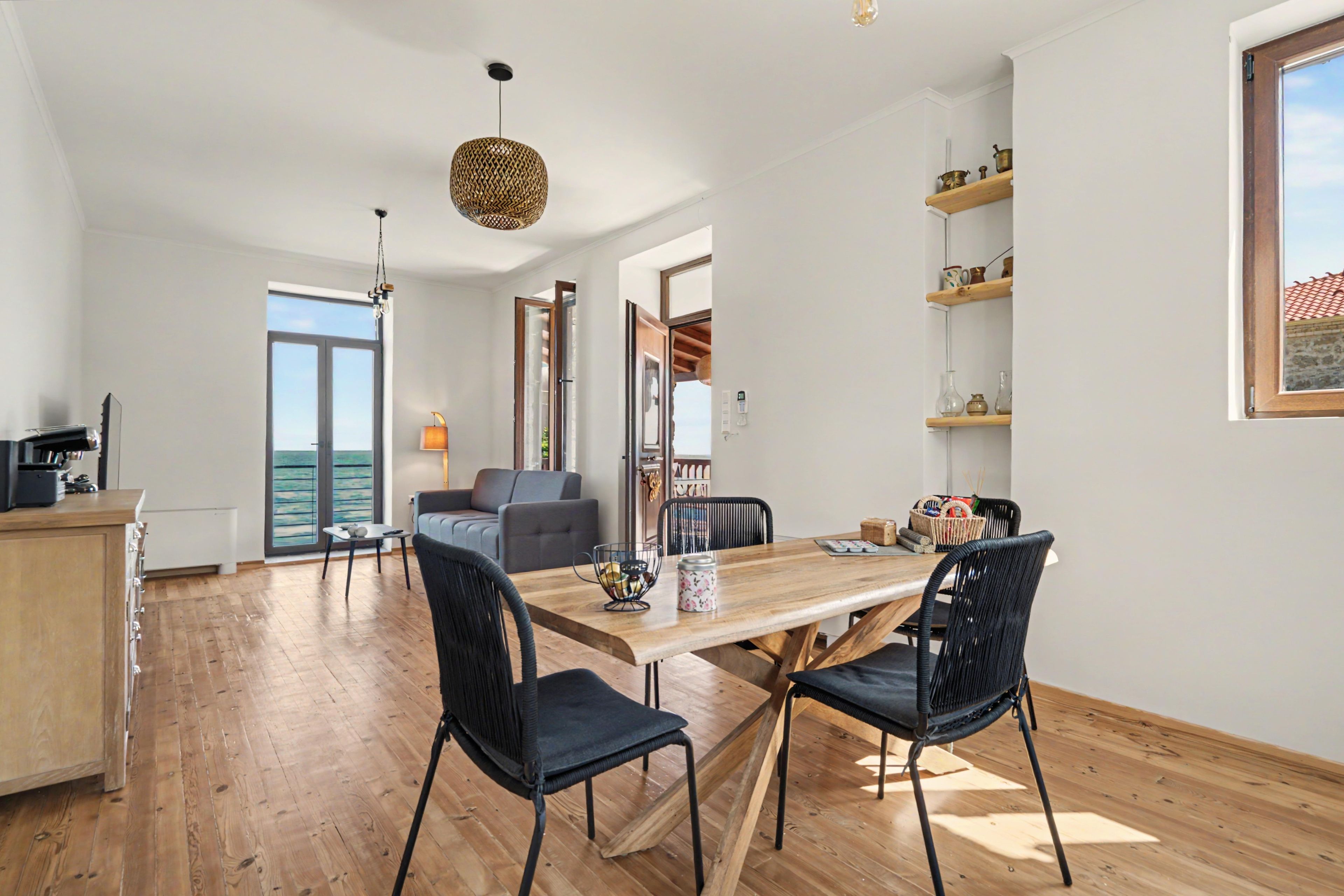 A spacious dining area with a wooden table and black chairs, a kitchen area with a wooden cabinet, and a view of the sea through large windows.