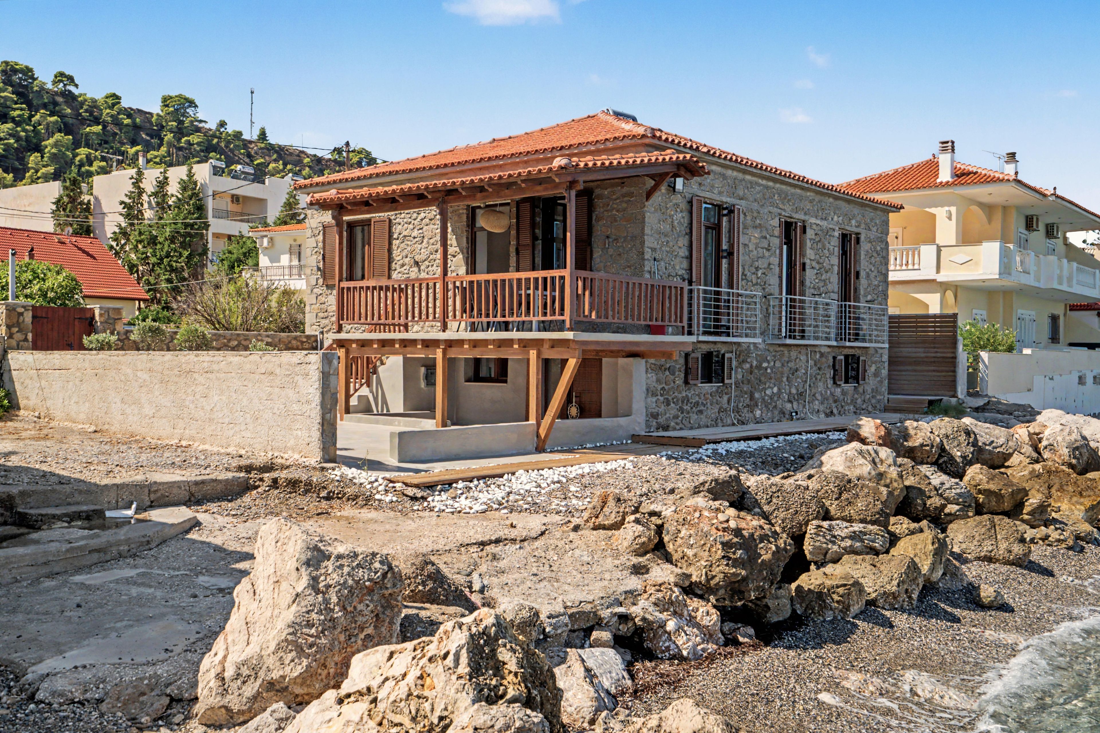 A stone building with a red-tiled roof, a wooden balcony, and a rocky foreground.
