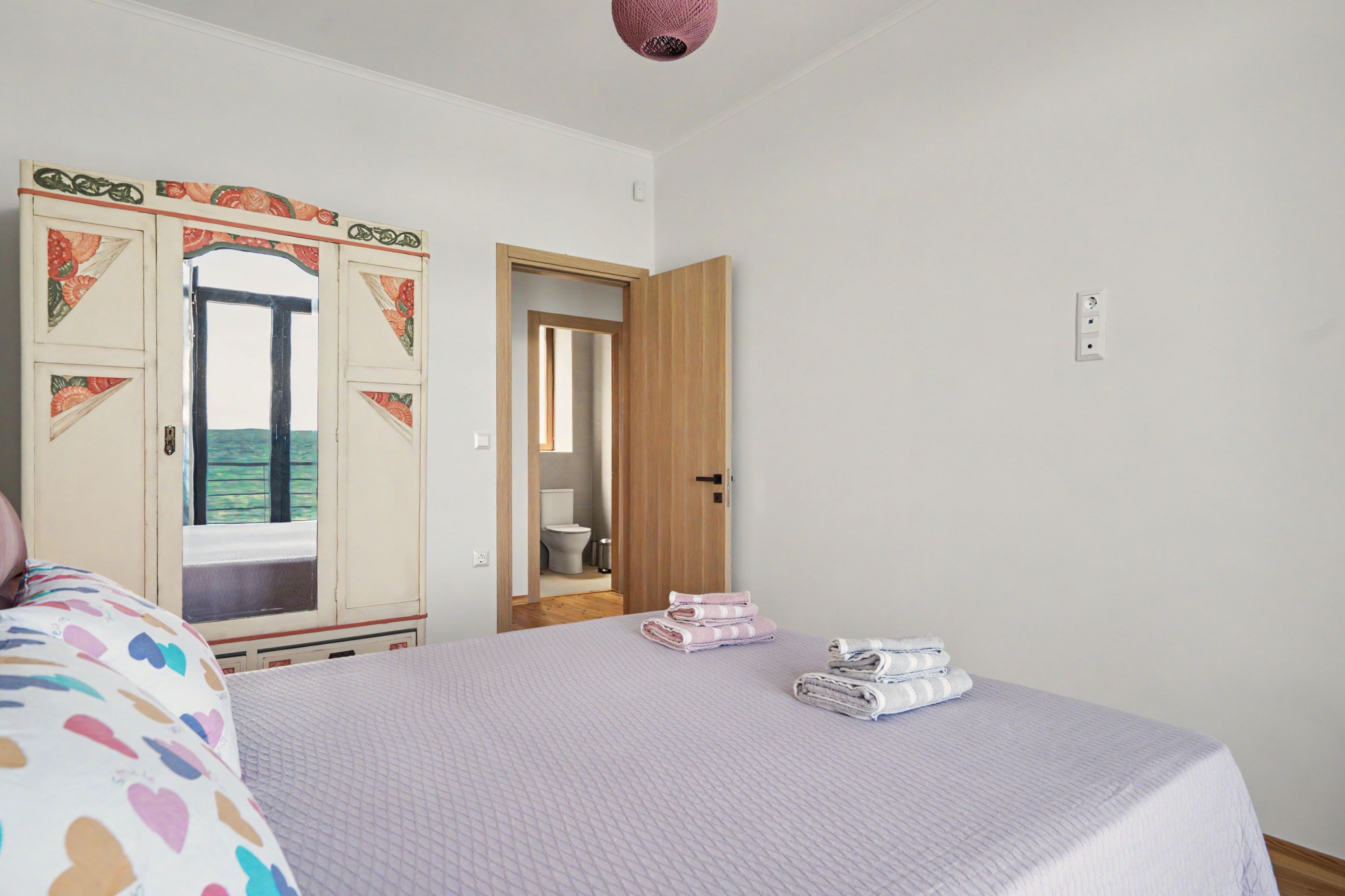 Una habitación con cama, armario y baño visible a través de una puerta abierta.