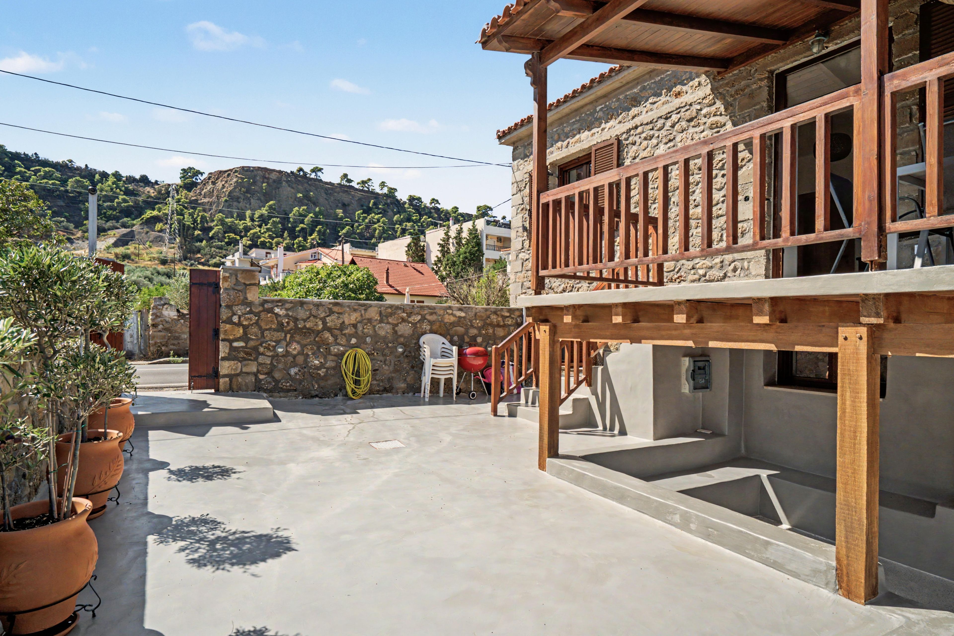 A residential building with a stone facade, wooden balcony, and a view of a hilly landscape.