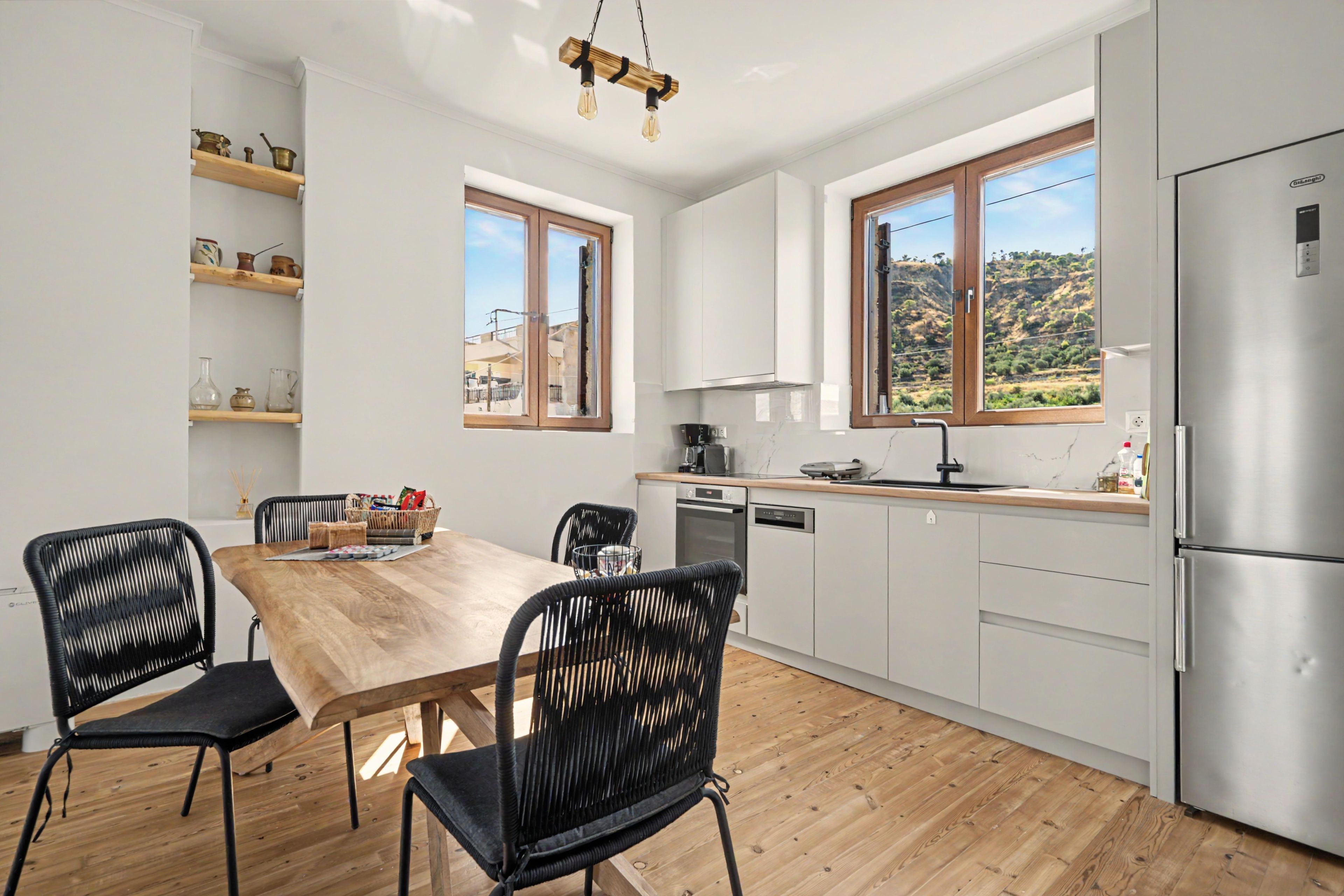 A modern kitchen with white cabinets, a wooden dining table, black chairs, and a stainless steel refrigerator.