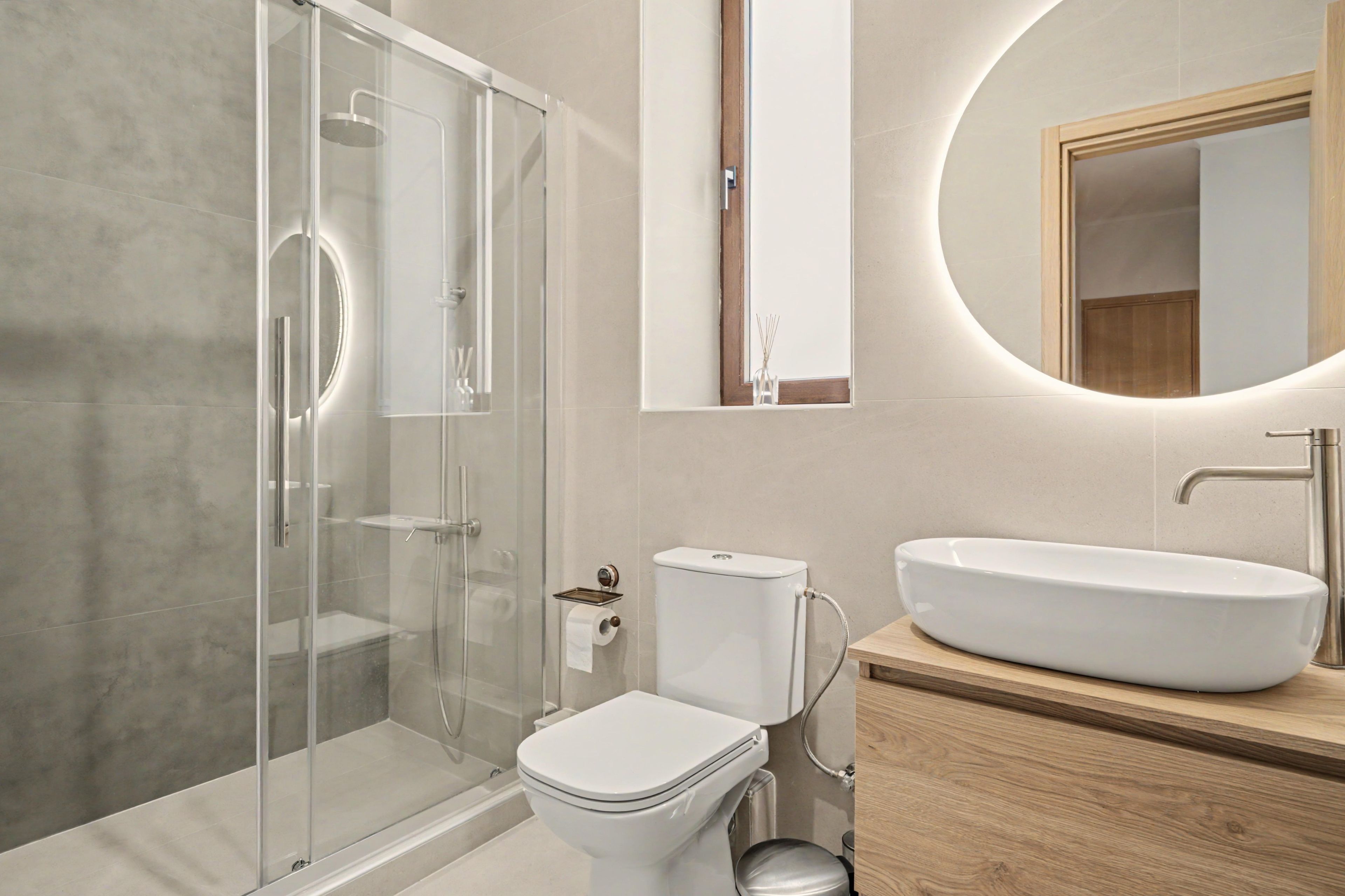 A modern bathroom with a glass-enclosed shower, a white toilet, and a wooden vanity with a large sink.