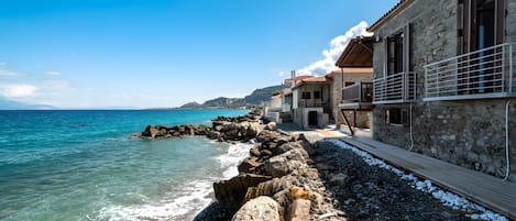 A coastal building with a stone facade, a wooden deck, and a view of the sea.