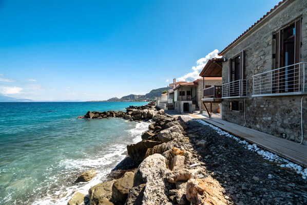 A coastal building with a stone facade, a wooden deck, and a view of the sea.