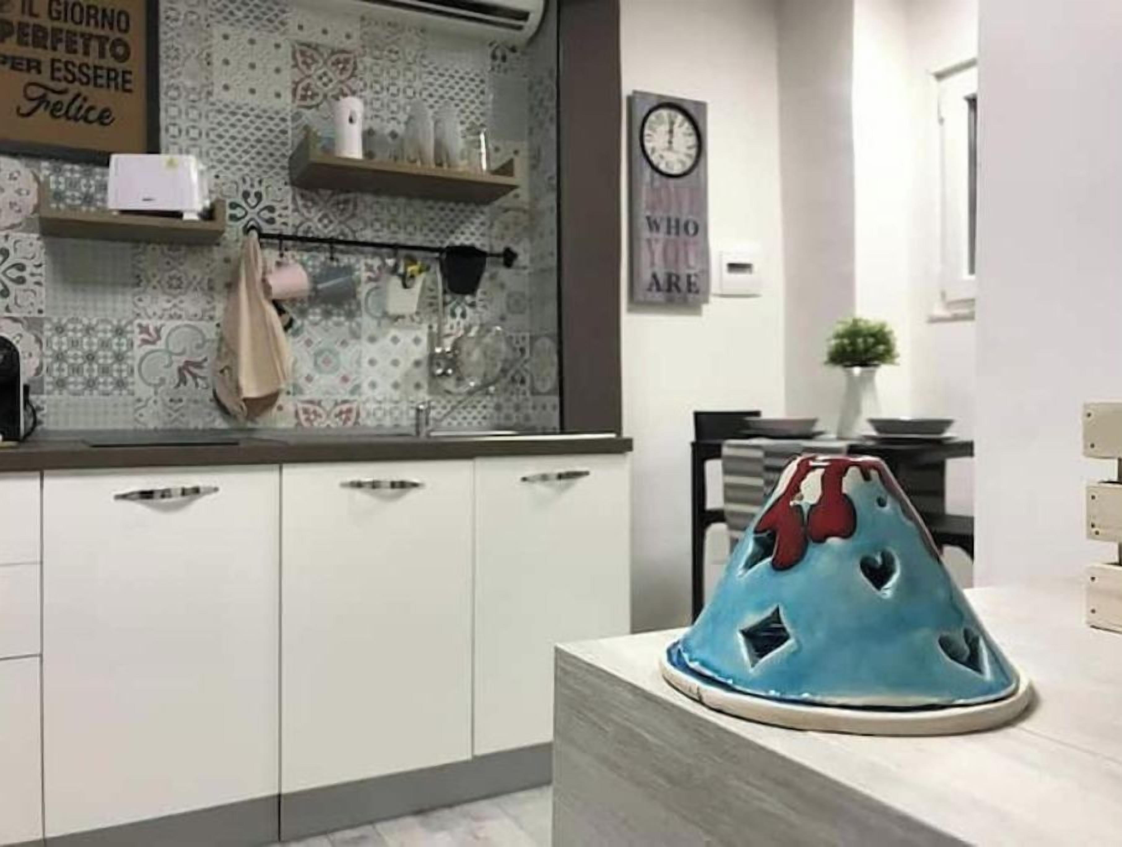 A kitchen with white cabinets, a blue decorative item on the counter, and a wall with a clock and a sign.