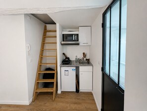 A compact kitchen with a microwave, a small refrigerator, and a wooden ladder. - Cozy Studio near Bastille, République & Marais (Paris)