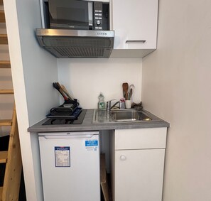 Eine kompakte Küchenzeile mit Mikrowelle, kleinem Kühlschrank, Spüle und verschiedenen Küchenutensilien.