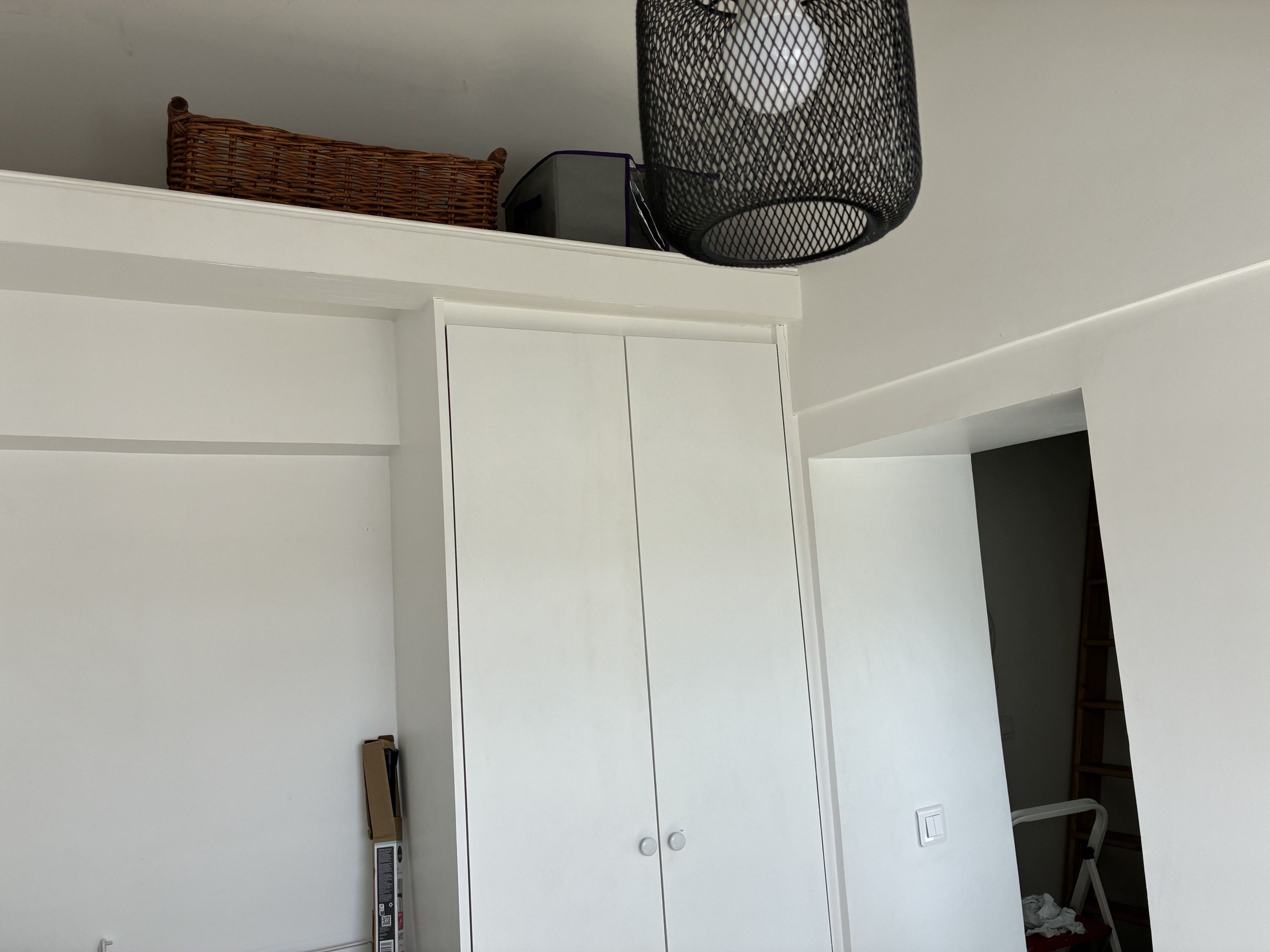 Een witte kast met een handgreep, een rieten mandje bovenop en een zwarte hanglamp.