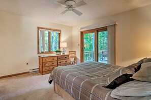 Ein Schlafzimmer mit Bett, Kommode, Lampe und Blick ins Freie durch ein Fenster.