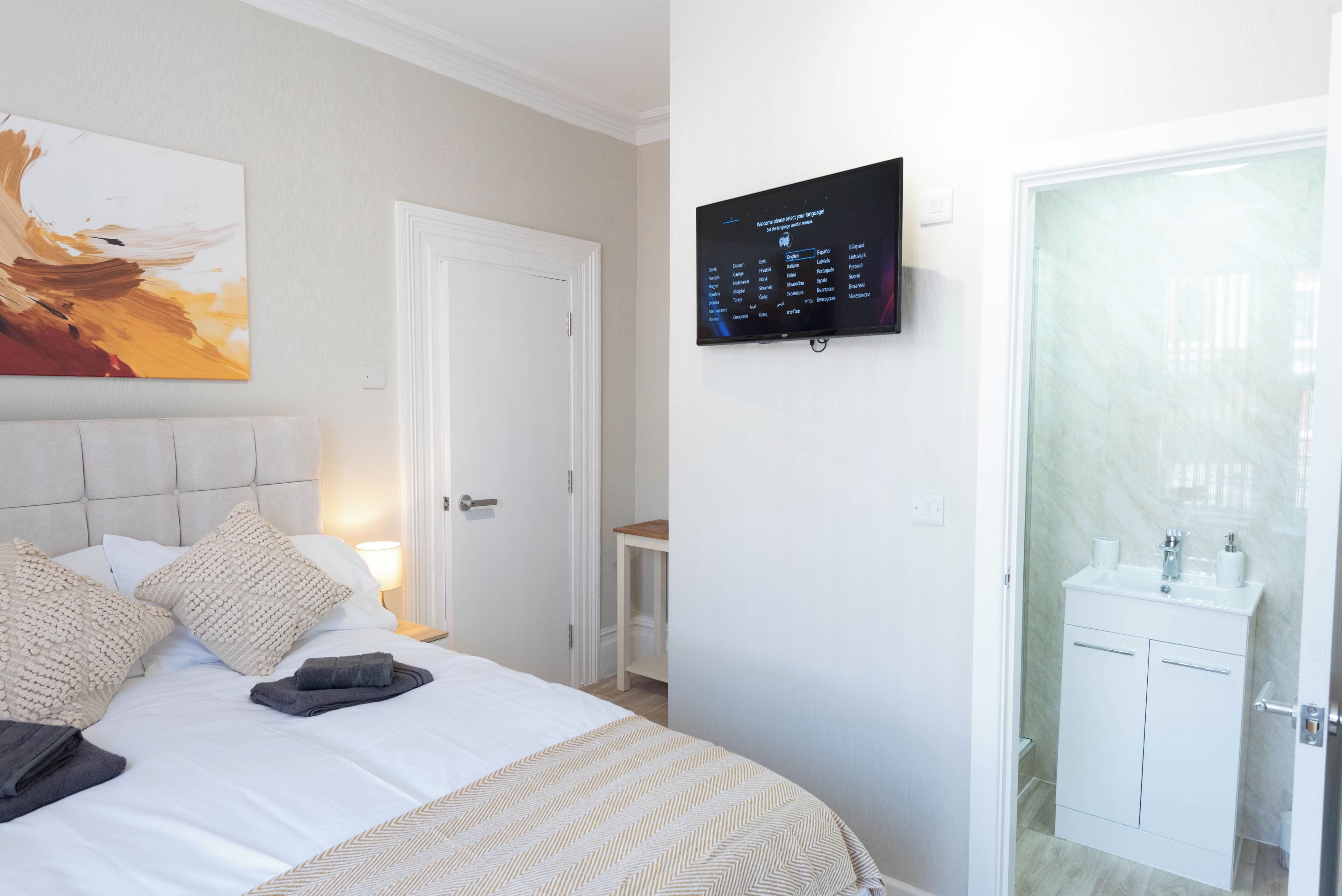 Ein Hotelzimmer mit einem Bett, einem an der Wand befestigten Fernseher, einer Tür und einem Badezimmer mit Waschbecken und Spiegel.