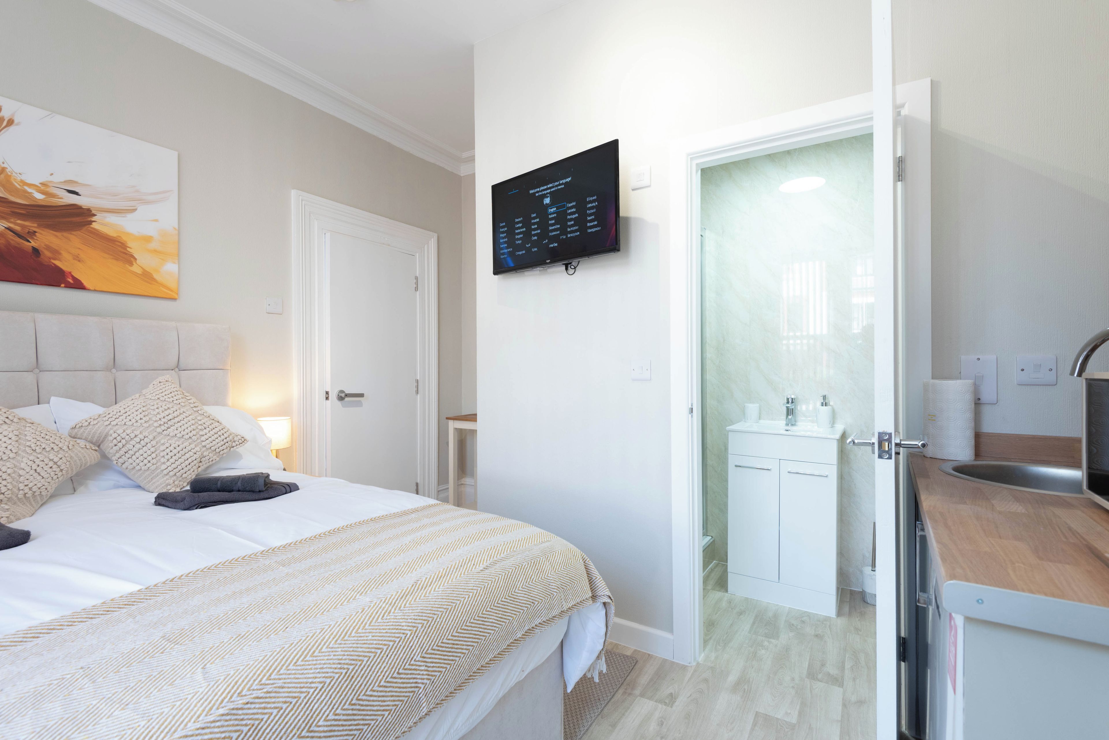 Une chambre d’hôtel avec un lit, un téléviseur fixé au mur, une porte donnant sur une salle de bain et une petite table avec une lampe.