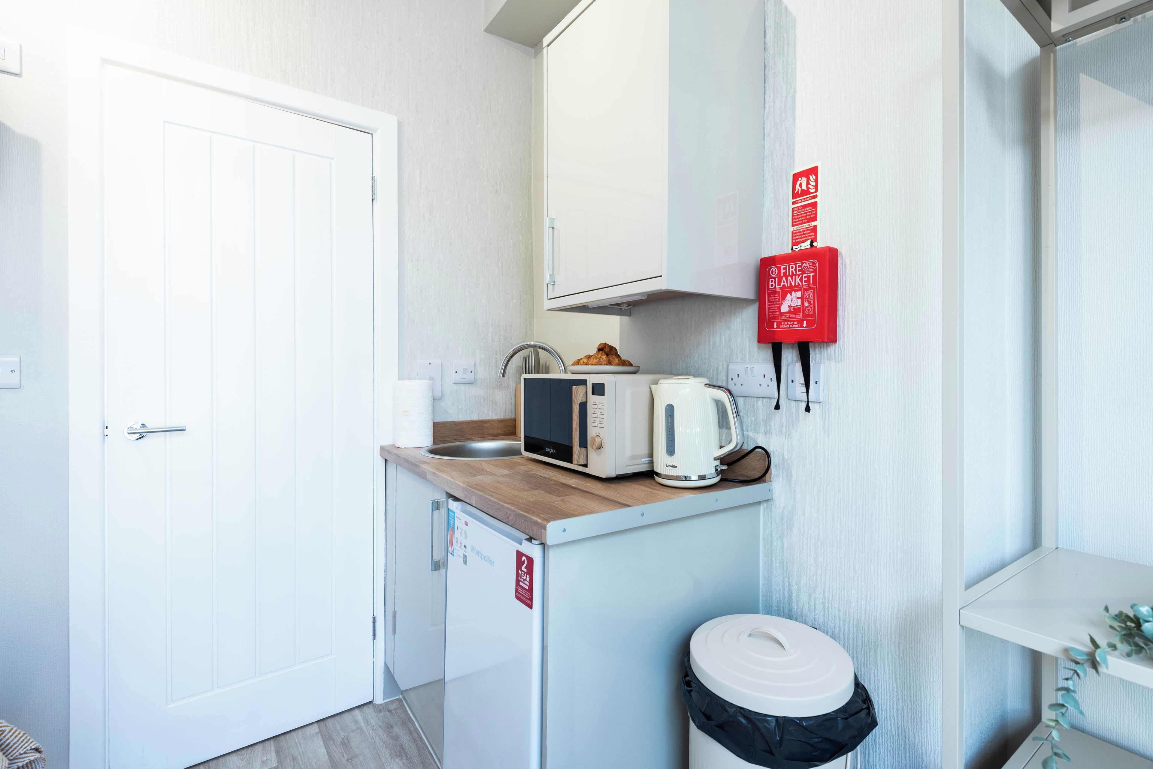 Una kitchenette compacta con microondas, tostadora y un pequeño cubo de basura.
