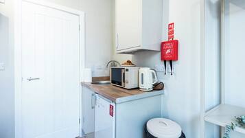 Una kitchenette compacta con microondas, tostadora y un pequeño cubo de basura.