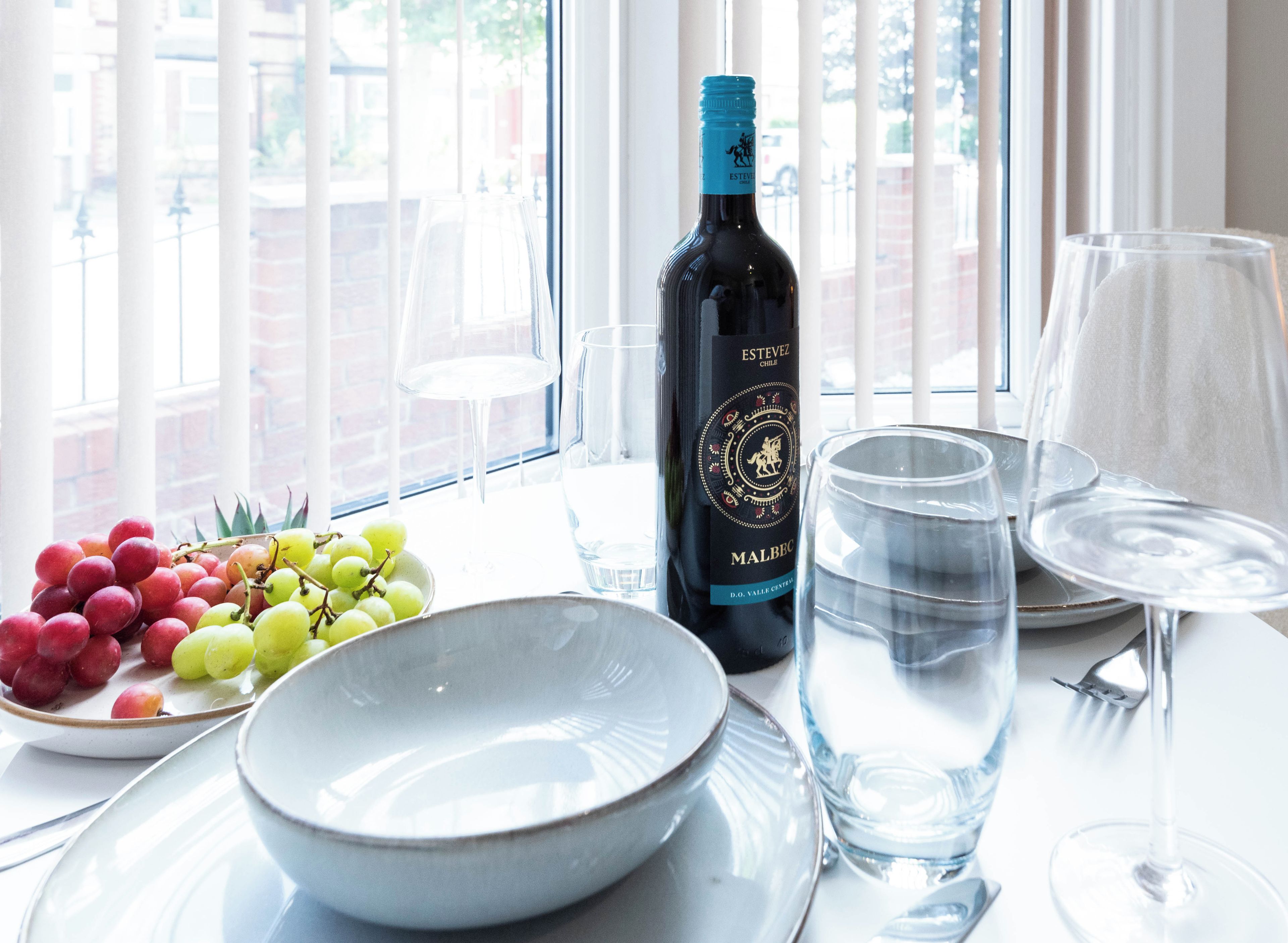 Una mesa con una botella de vino, un cuenco de uvas y dos vasos de agua.