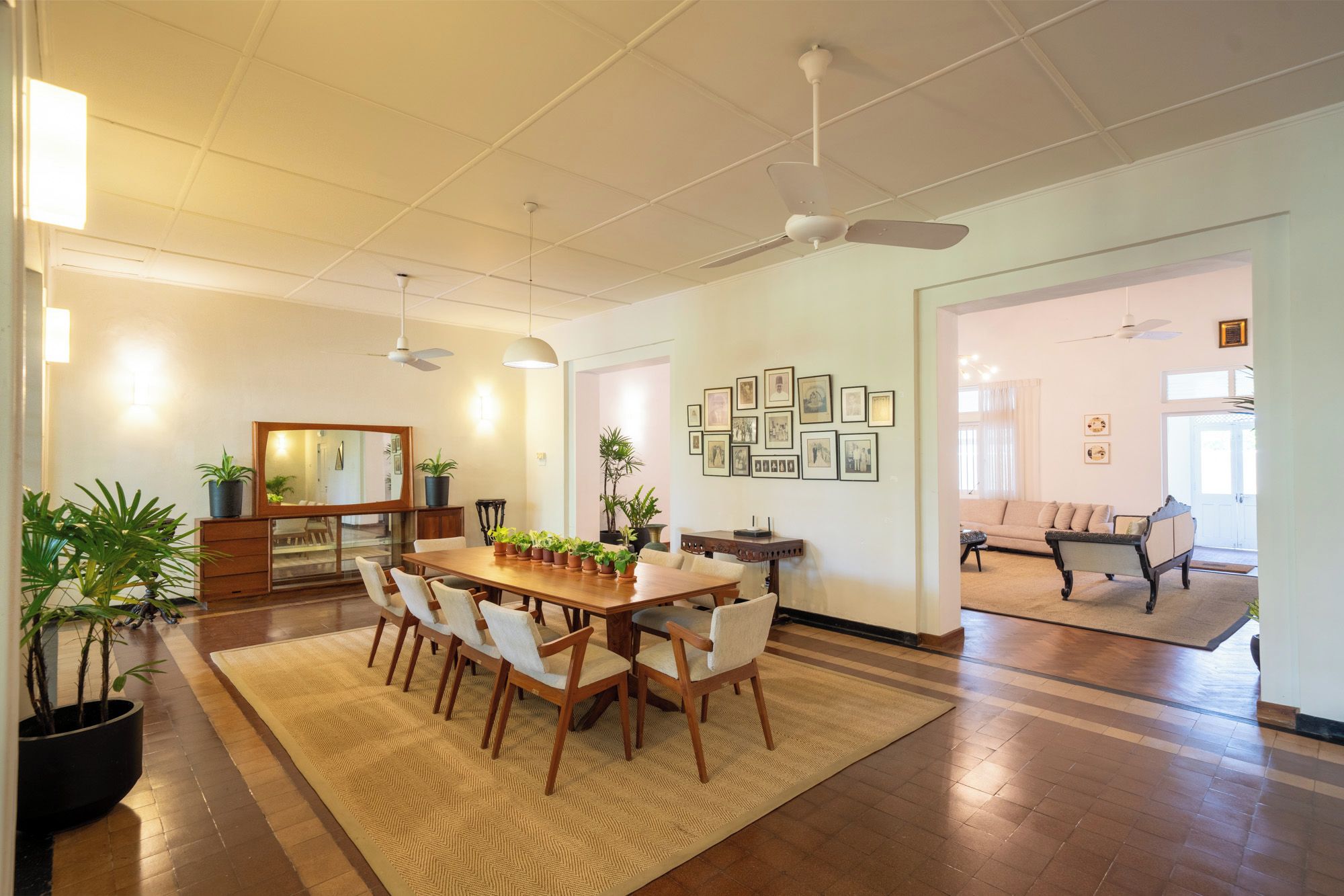 A spacious dining area with a wooden table and chairs, surrounded by potted plants.