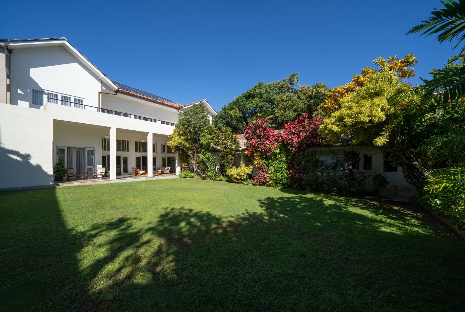 A modern house with a covered patio, a well-maintained lawn, and a variety of colorful plants.