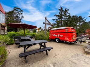 Ein roter Food-Truck mit dem Schriftzug 'Village Scoop', geparkt in der Nähe von Picknicktischen und einem Sonnenschirm.