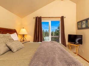 Quarto com cama, televisão em móvel, janela com cortinas e vista para árvores.