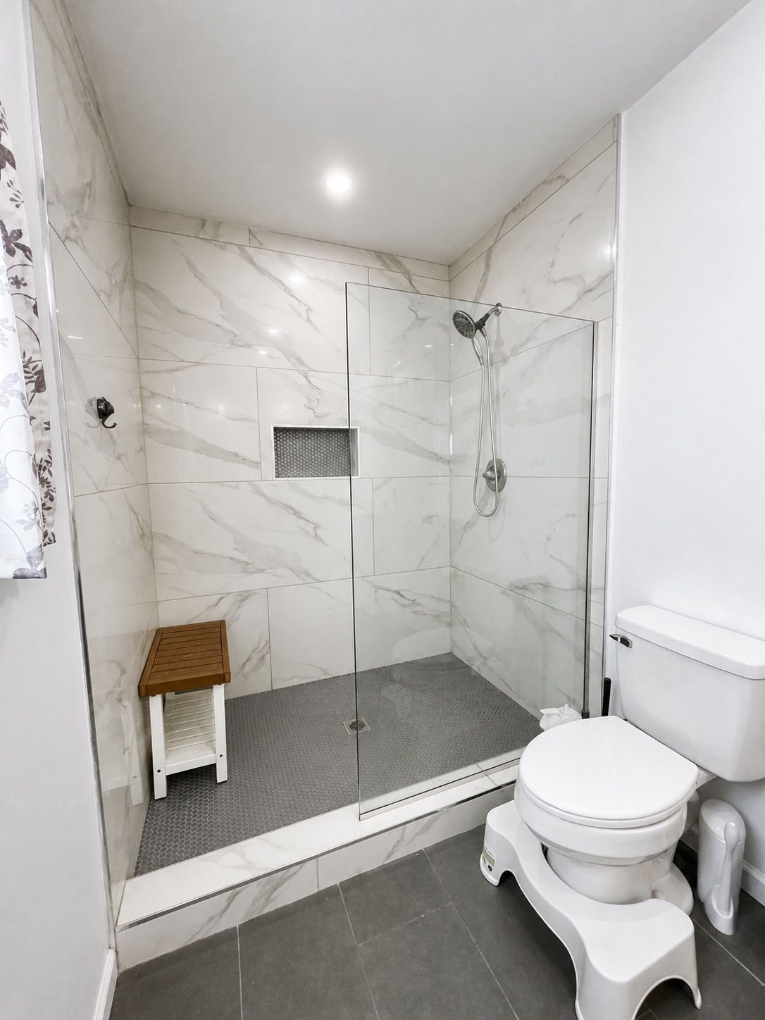 Un baño moderno con ducha envuelta en cristal, un taburete de madera, un inodoro y un bidé.