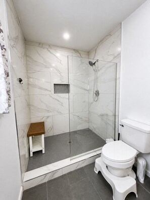 Une salle de bain moderne avec une douche à parois de verre, un petit tabouret en bois, des toilettes et un bidet.