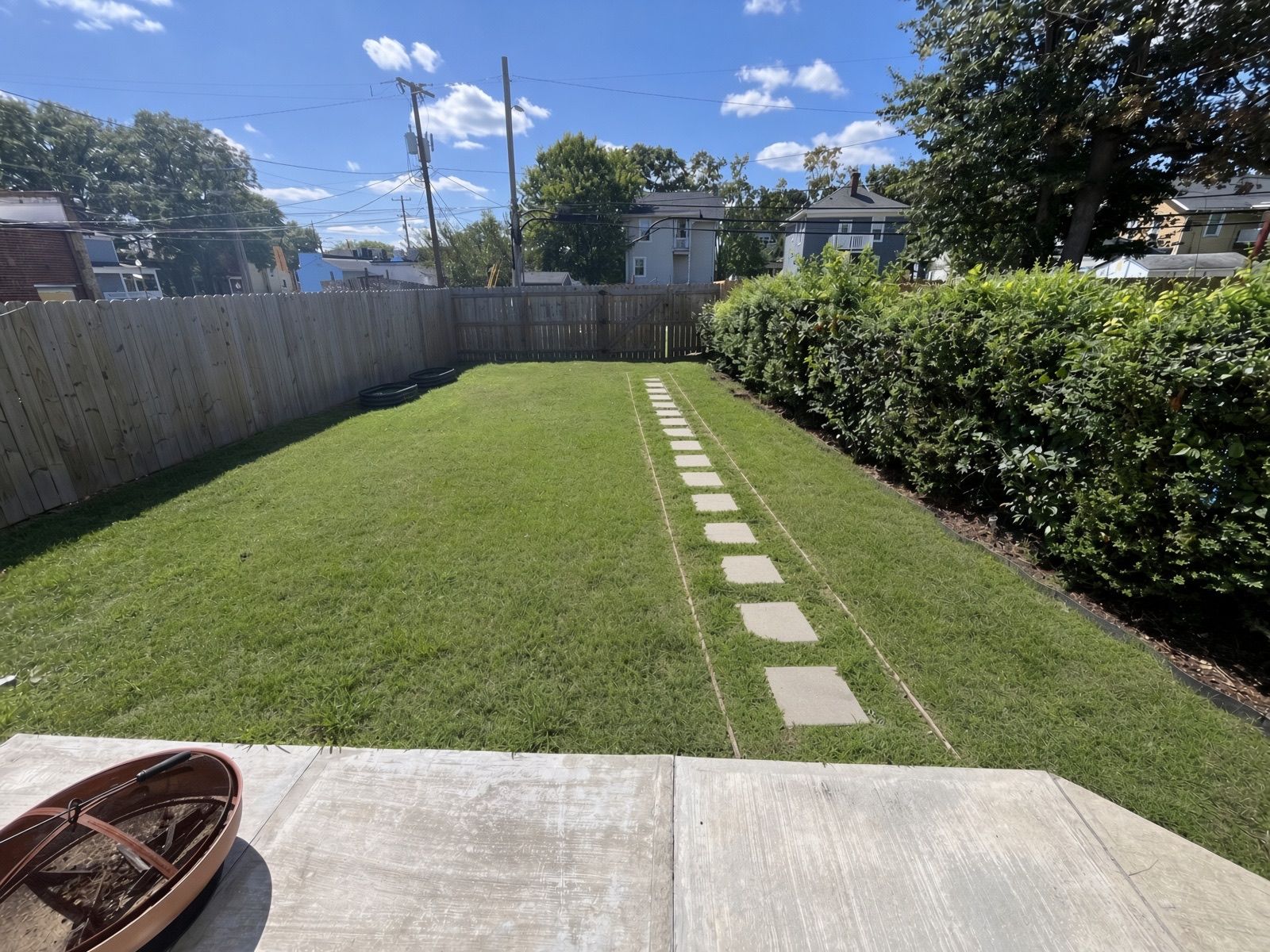 A backyard with a paved path, a wooden deck, and a hedge.