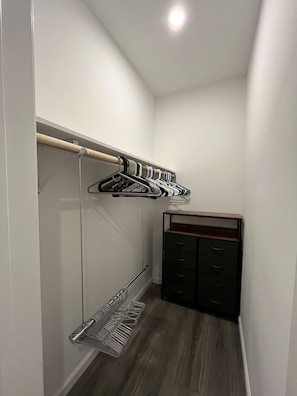 Un couloir étroit doté d’un plancher en bois, d’une armoire avec des tiroirs de couleur foncée et d’un portant à vêtements muni de plusieurs cintres.