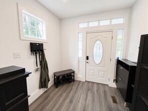 Ein Zimmer mit einer Bank, einem Kleiderhaken, einer Tür mit Glasfenster und einem Fenster.
