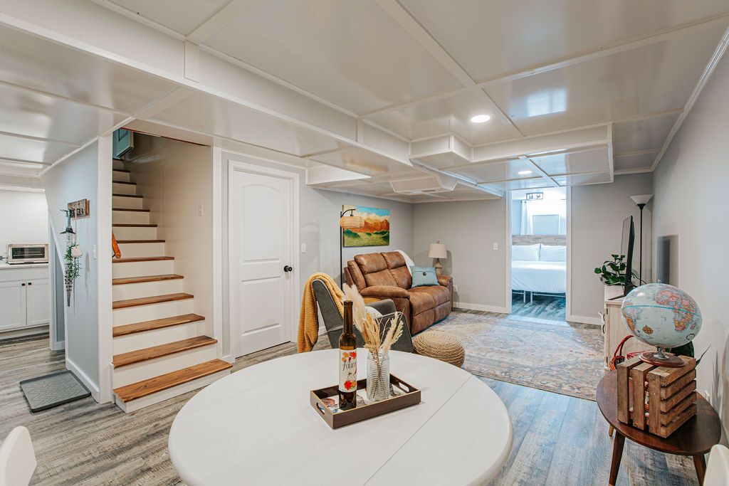 A spacious living area with a staircase, a brown leather sofa, a globe on a wooden stand, and a dining table with a tray.