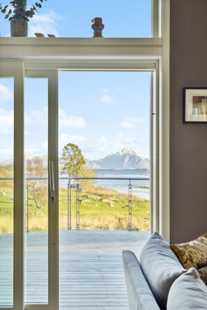 A room with a sliding glass door leading to a balcony with a view of a lake and mountains.