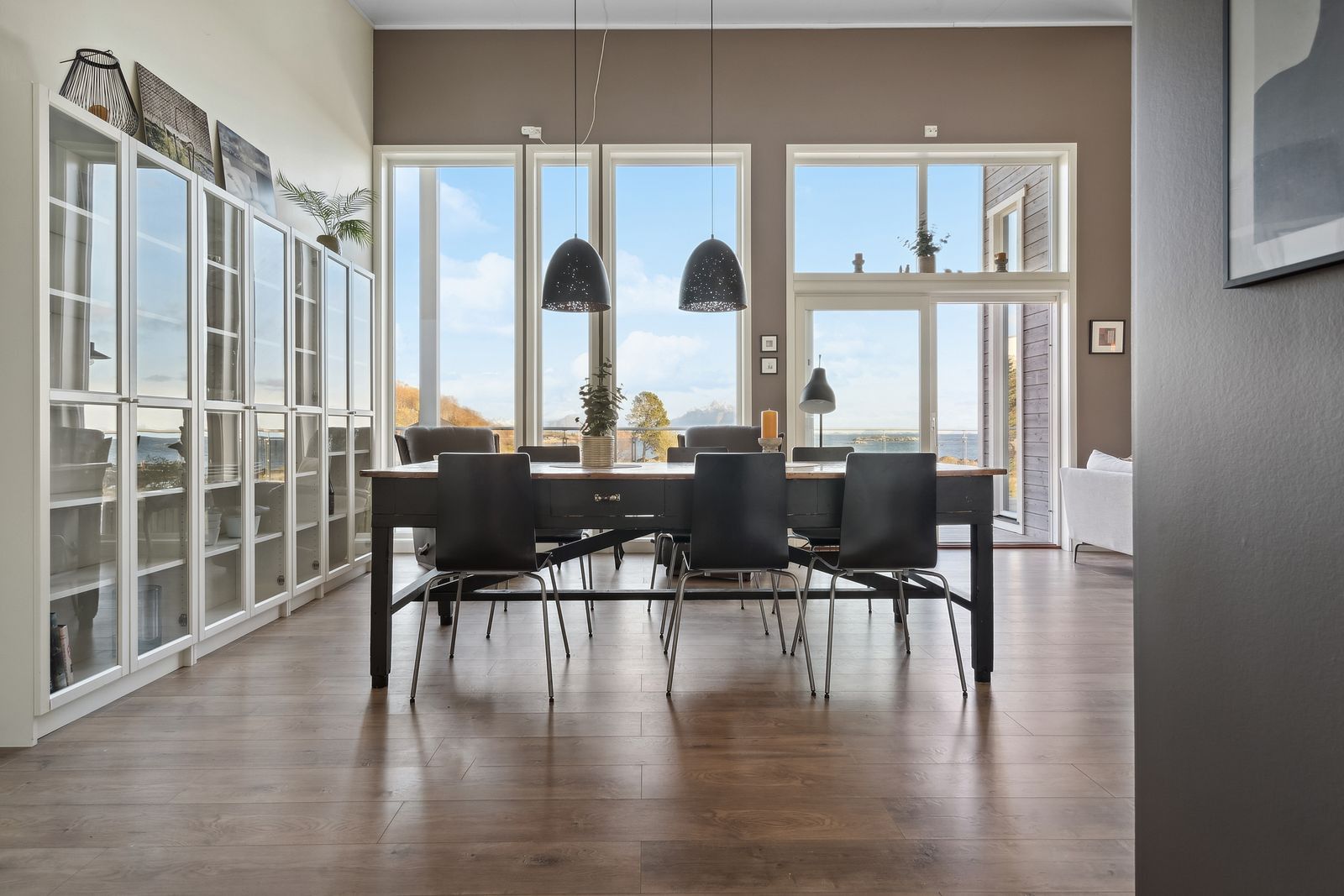 Un espace repas avec une table en bois, des chaises noires et des luminaires suspendus.